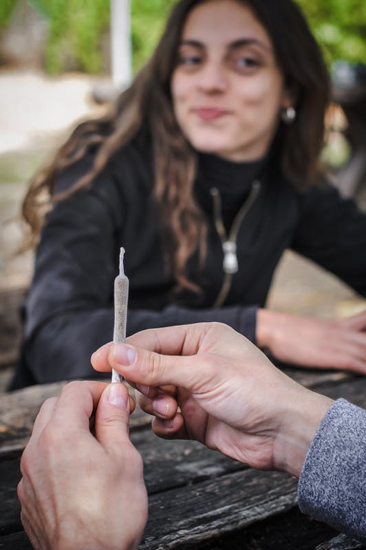 hand holding a joint with a lady looking