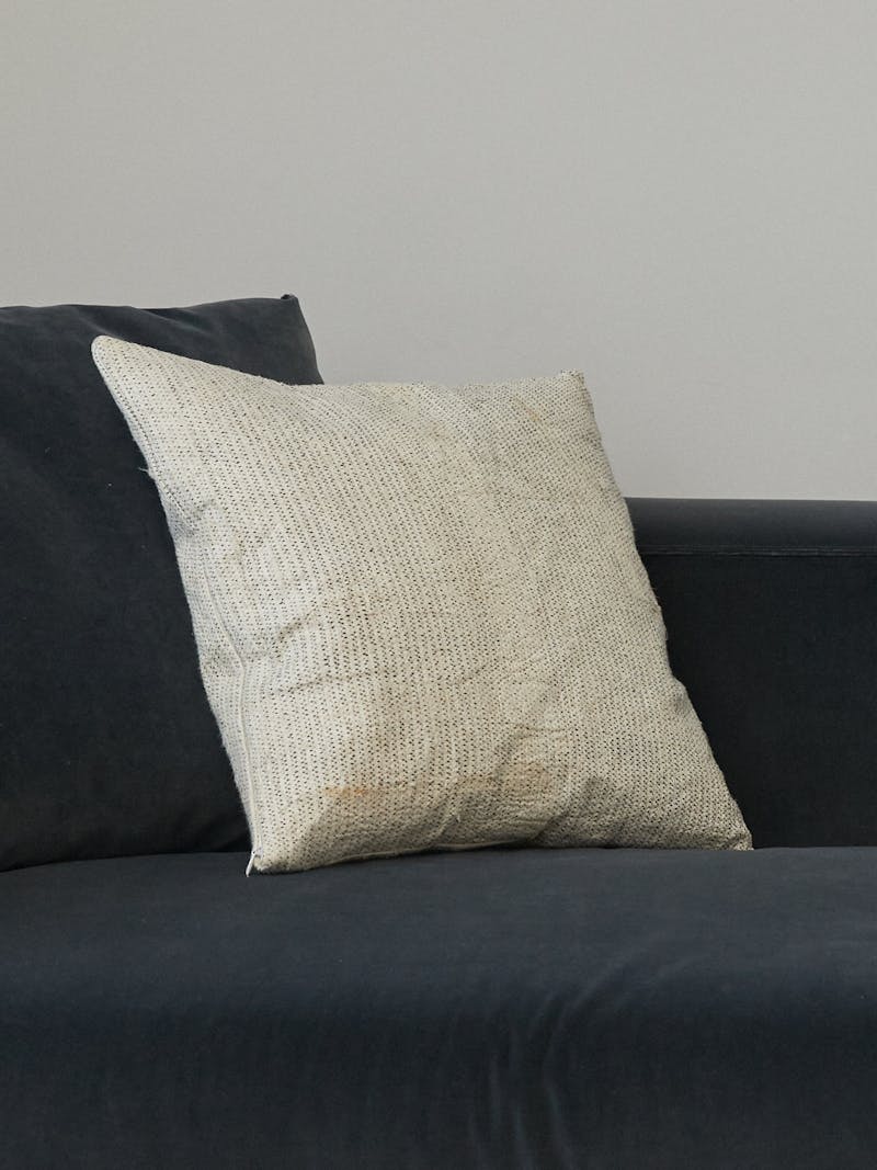 wooden tapa cloth textile pillow by Amsterdam based Buro Belen. The pillow is a cream colour with black cotton stitching and sits on a blue velvet sofa. 