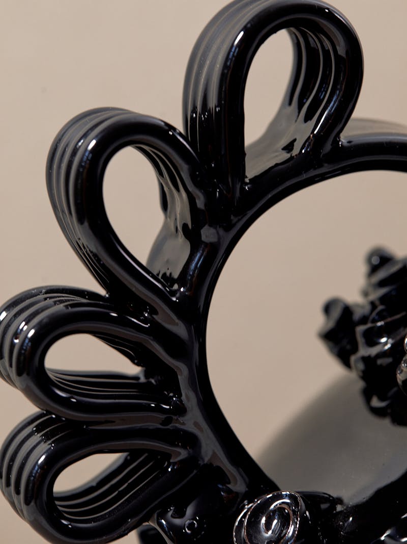 Detail shot of black glossy glazed terracotta vase with curved ribbon-like handles. 