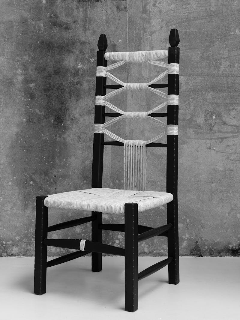 Black and white image displaying the Nannai Chair from the 'scannu' series by Pretziada. The material is made from chestnut wood and contains woven decorative elements. The object is part of the new 2024 spring collection 'Observations' by online gallery Metamorphoses Objects.