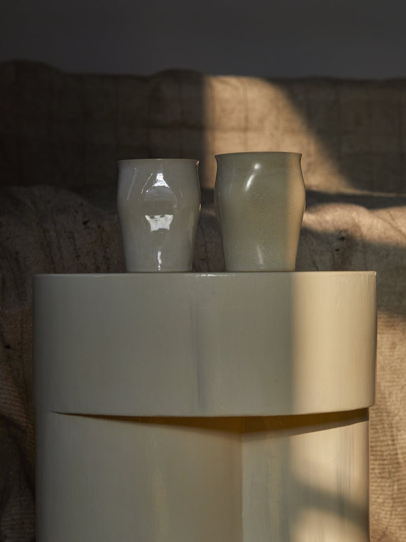 Two unique handmade cream coloured ceramic curved cups are shown next to each other from Russian designer Maria Tyakina. The vessels sit on a horn side table from destroyers/builders