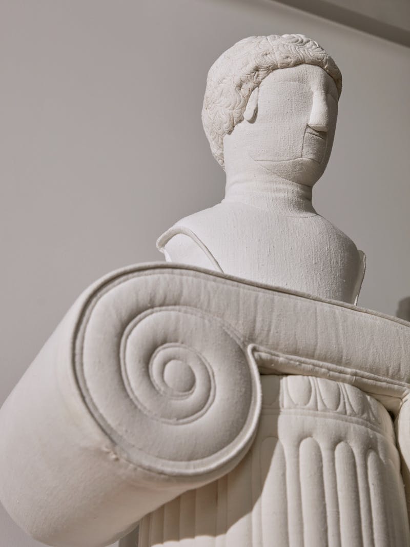 The top of an ionic pillar or pedestal as a stitched linen sculpture, a textile bust sits on top of the pillar. Both works shown are by Spanish artist and designer Sergio Roger.  