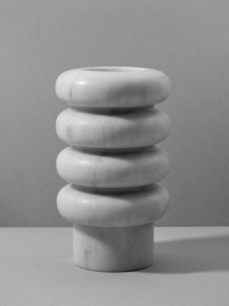 A black and white image of a carved marble vase that has cylindrical rings stacked on top of each other with a straight base. 