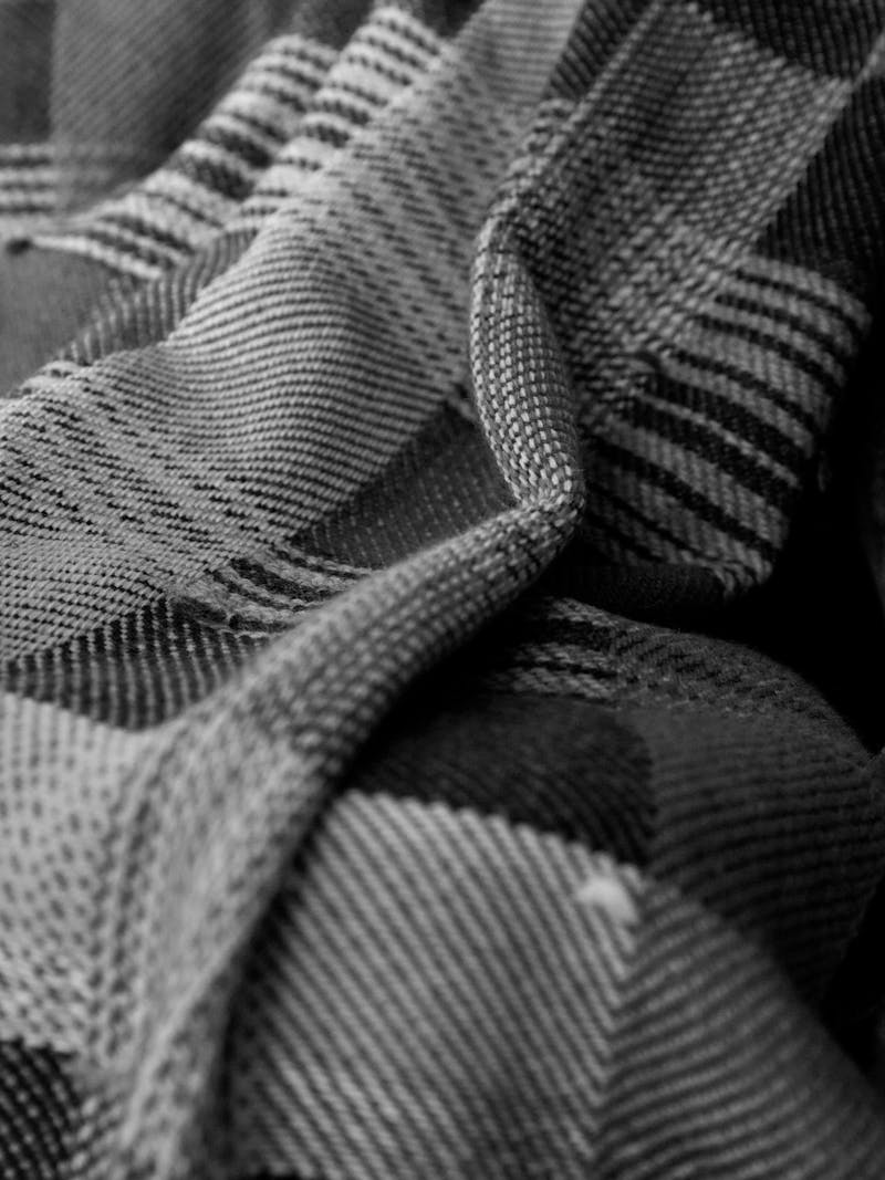 Black and white image of a unique hand woven alpaca blanket with a plaid and checkered pattern in brown, camel, black and rust colours. 