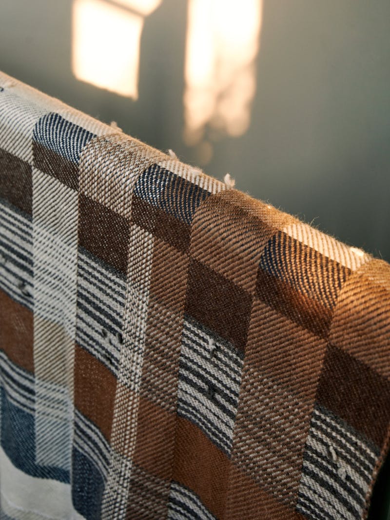 A unique hand woven alpaca blanket with a plaid and checkered pattern in brown, camel, black and rust colours. 