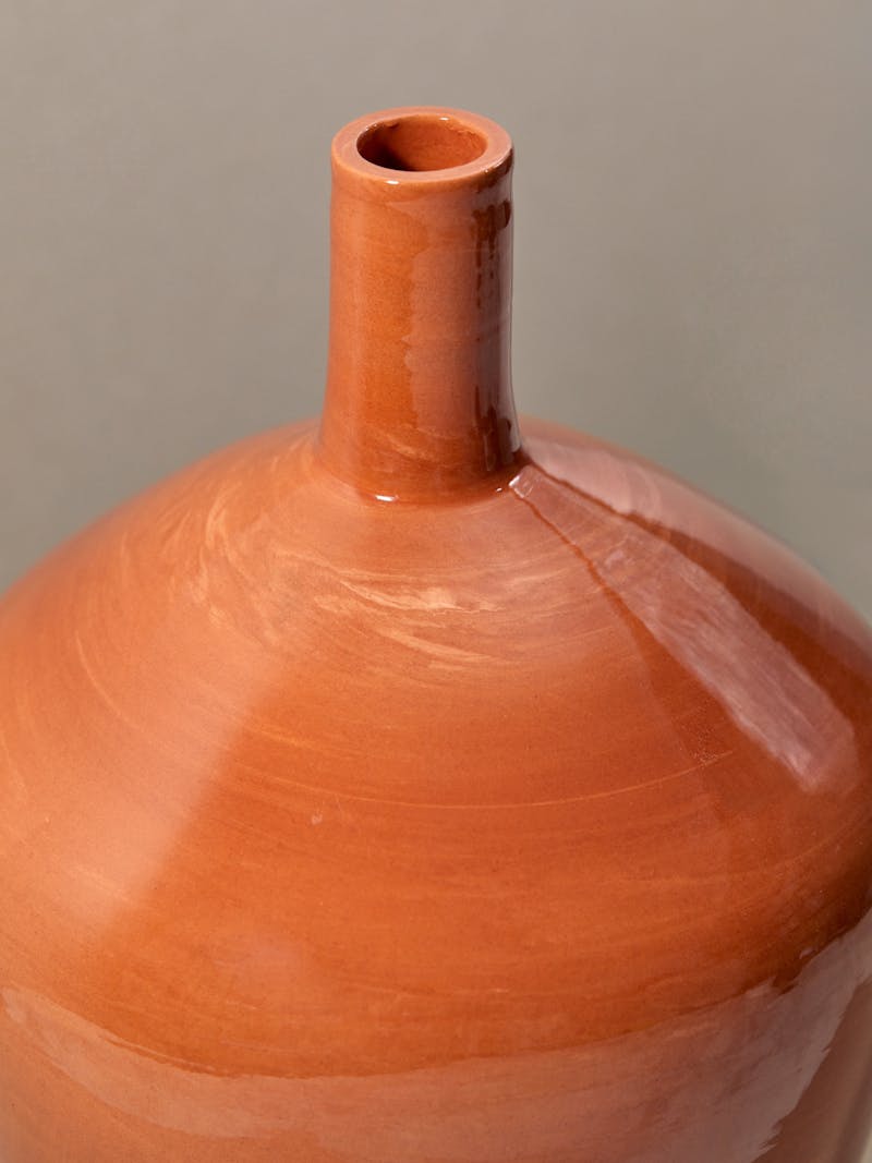 detail image of glazed orange terracotta ceramic urn with a wide body and slim neck.