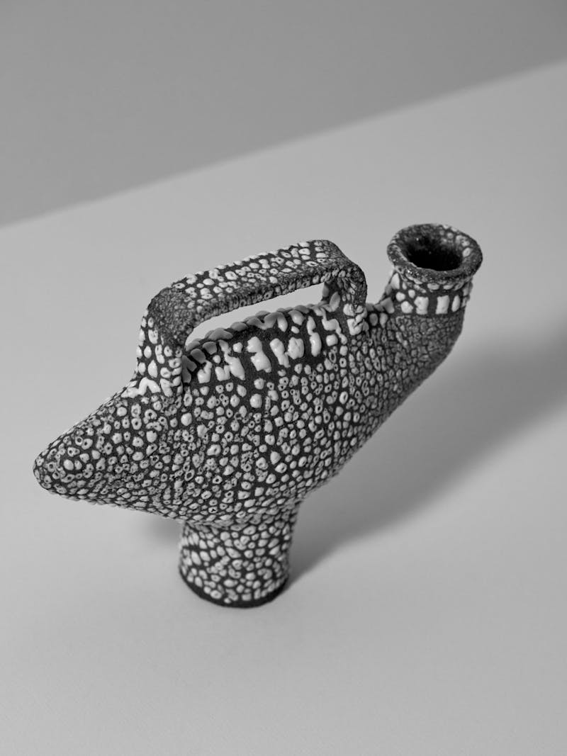 black and white photo of a glazed stoneware ceramic vessel by artist Catherine Dix. The glaze is irregular in texture and raised like volcanic rock, the body of the vessel is curved with a small foot. 