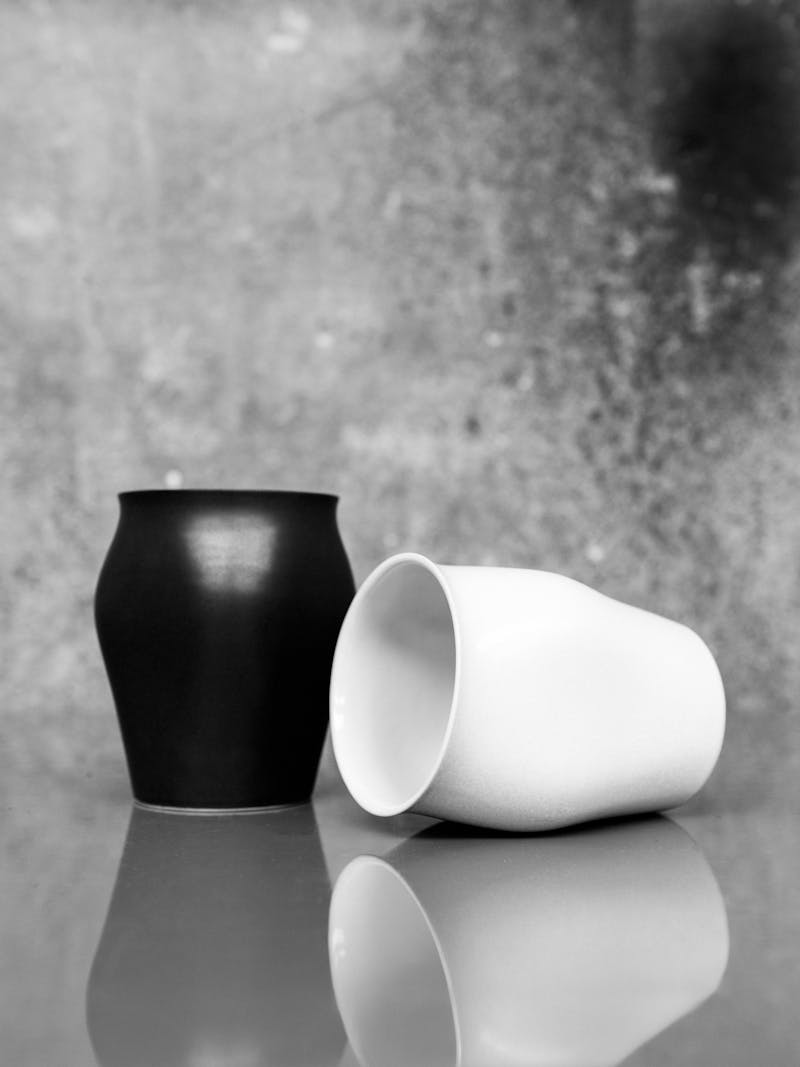 Black and white image displaying Cup One and Two by Maria Tyakina. The ceramic cups are included in black (left) and white (right). The objects are part of the new 2024 spring collection 'Observations' by online gallery Metamorphoses Objects.