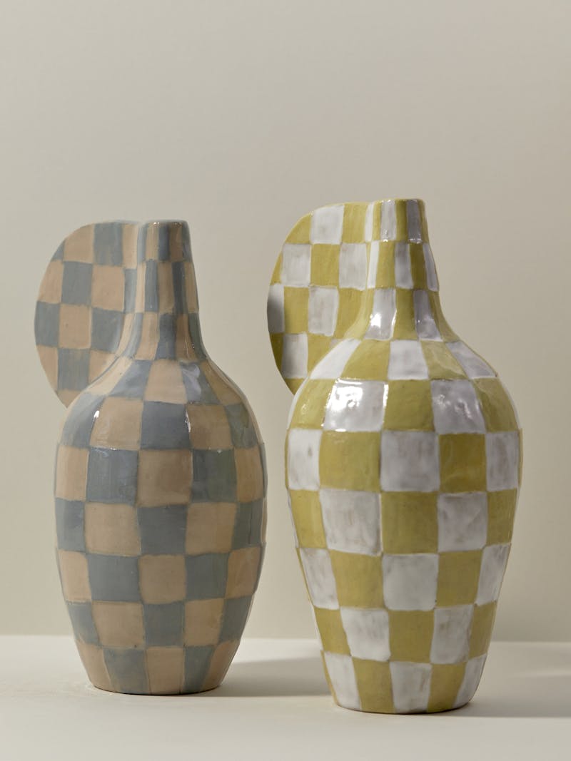 Two checkered ceramic objects by Maria Lenskjold, one is white and yellow and the other is blue and beige.