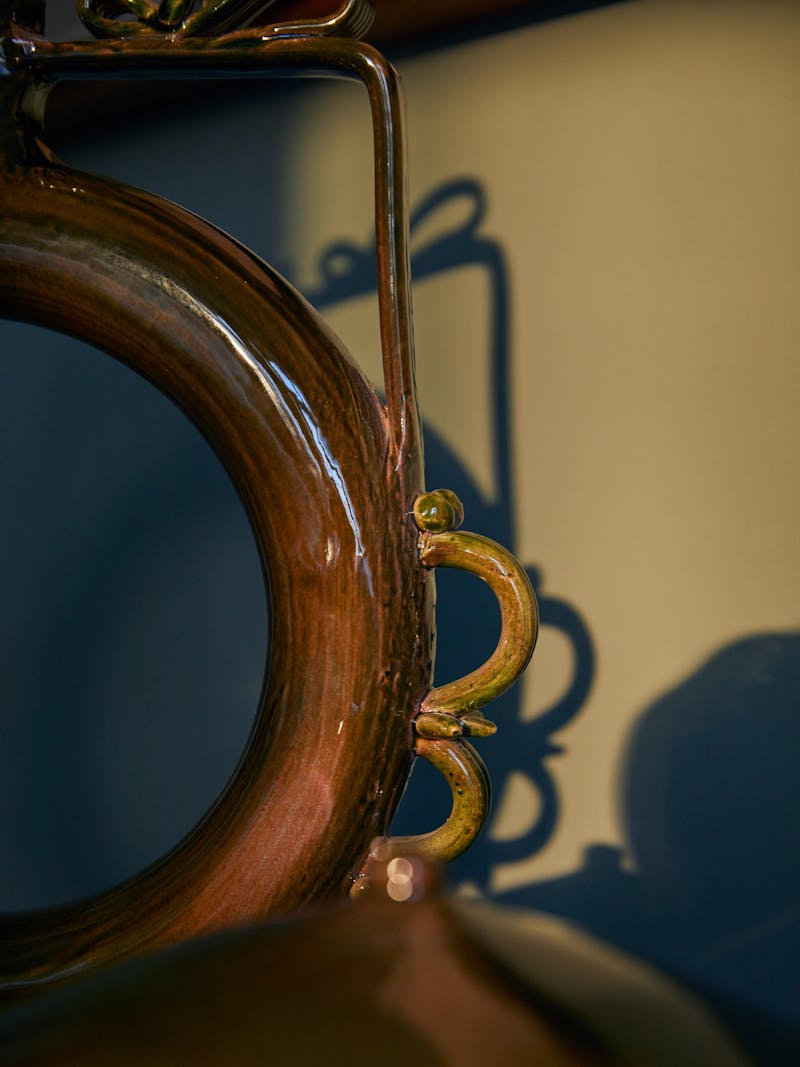 shadowy and high contrast detail image of a circular ceramic glazed vessel with decorative elements on the handles