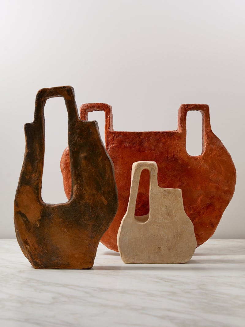 a set of three flat ceramic vessels from artist, designer and craftsman Willem van Hooff they are brown, cream and orange in colour and sit on a marble table top by de Padova.