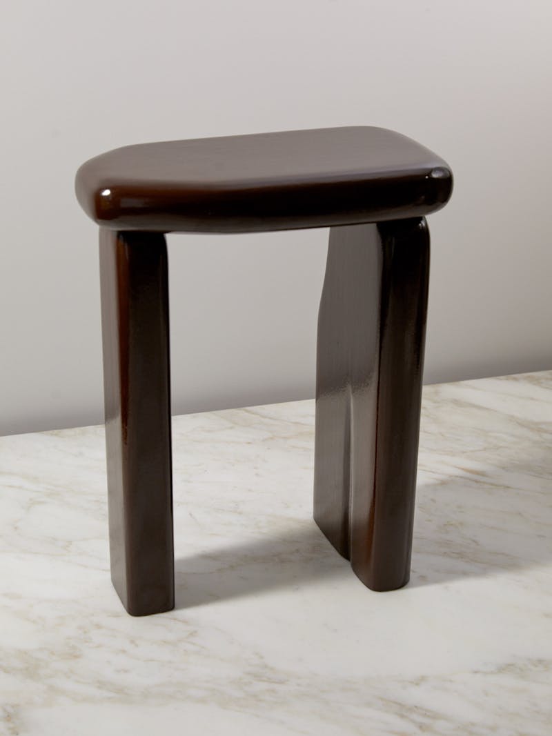 Architectural lacquer side table in dark red, burgundy, two organically shaped legs support one rounded flat oblong piece of lacquer, inspired by the forms of architect Lina Bo Bardi and designed by Destroyers/Builders. The table sits on a marble surface by de Padova. 