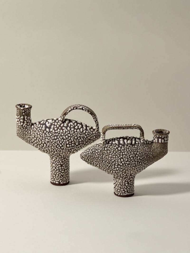 Set of two black and white textured glazed ceramic stoneware pieces by Catherine Dix. Each has a spout and handle, the body of the vessel is wide and oblong and the foot is narrow and long. 