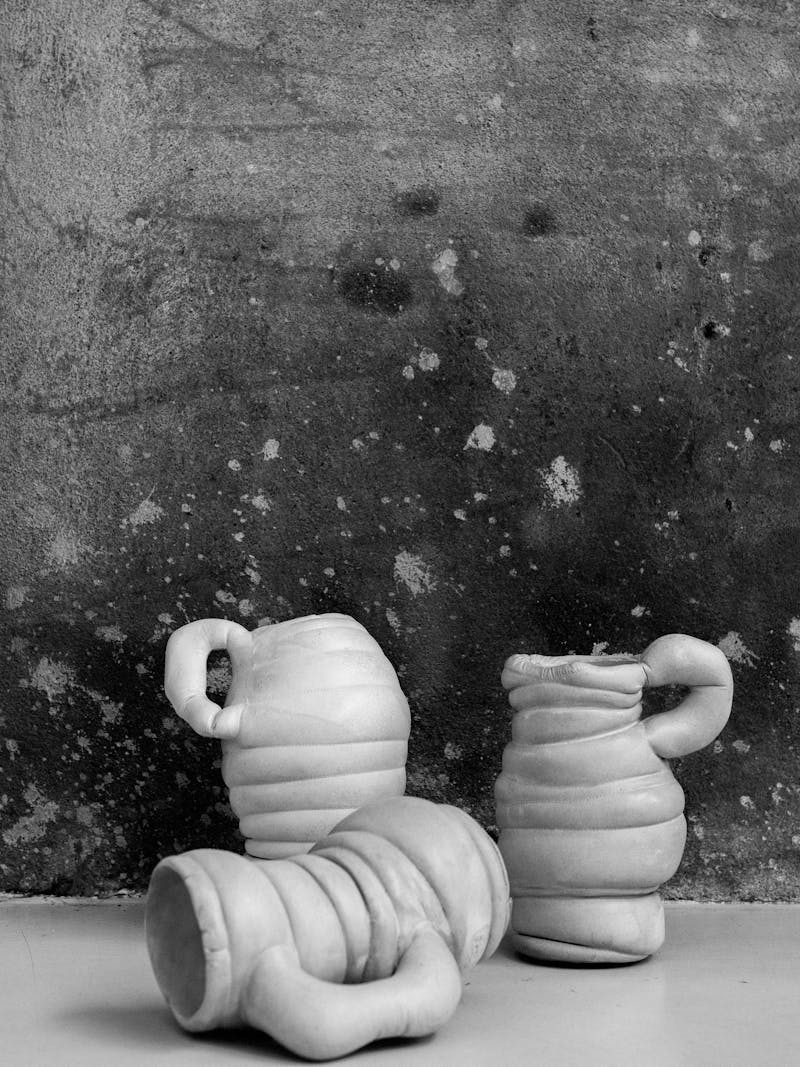 Black and white image displaying Chub Vase III by Tessa Silva. The vase is white and the body contains horizontal lines and a handle. The material is made using the 'Chalk & Cheese' technique which is produced by manipulating proteins in fermented skimmed milk. This object is exclusively made for the new 2024 spring collection 'Observations' by online gallery Metamorphoses Objects.