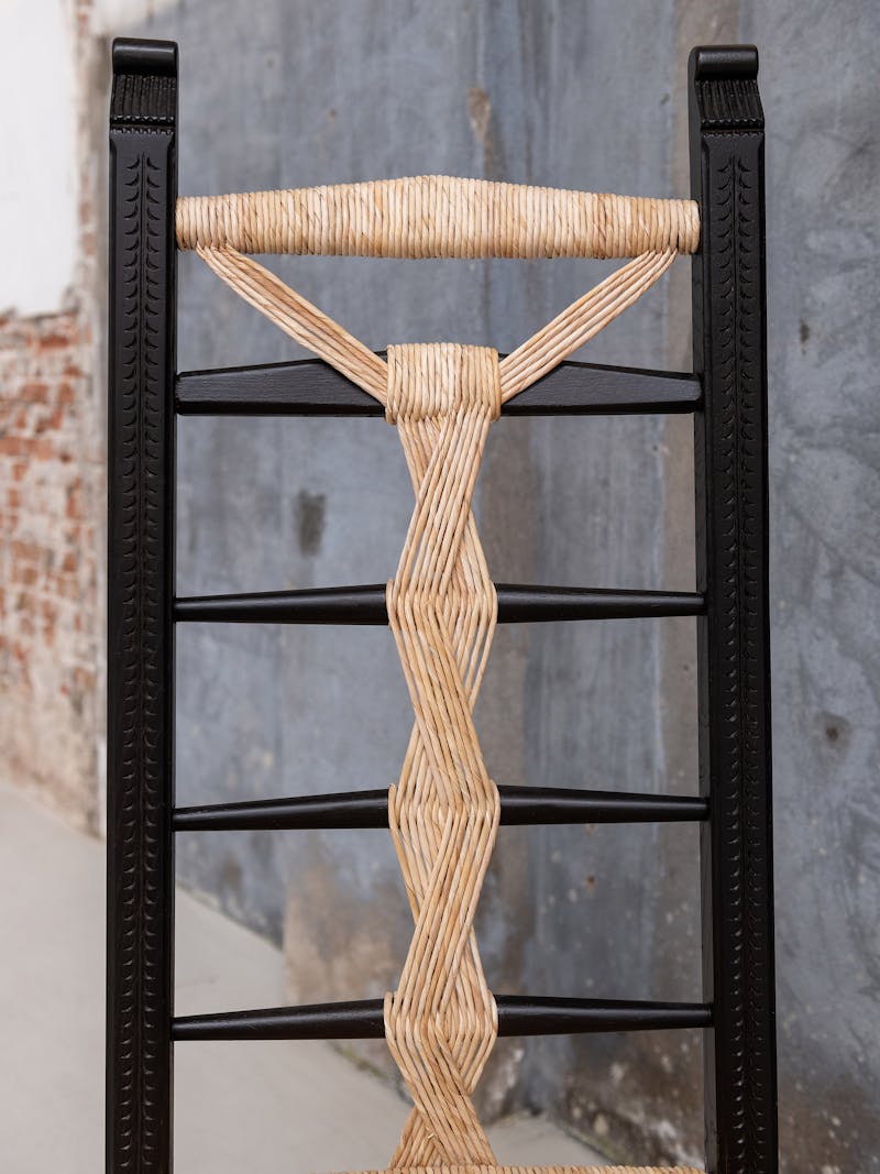 image displaying the Lia Chair from the 'scannu' series by Pretziada. The material is made from chestnut wood and contains woven decorative details. This object is part of the new 2024 spring collection 'Observations' by online gallery Metamorphoses Objects.