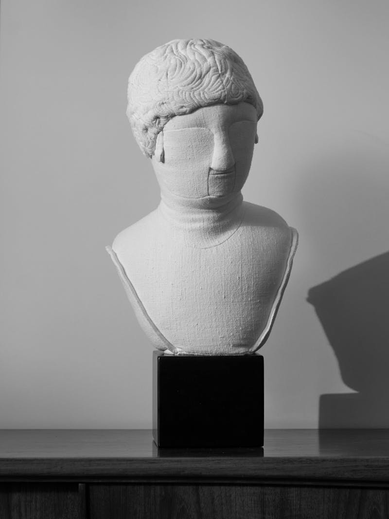 black and white image of an off white linen sculptural textile bust by Spanish designer Sergio Roger on a black cube plinth.