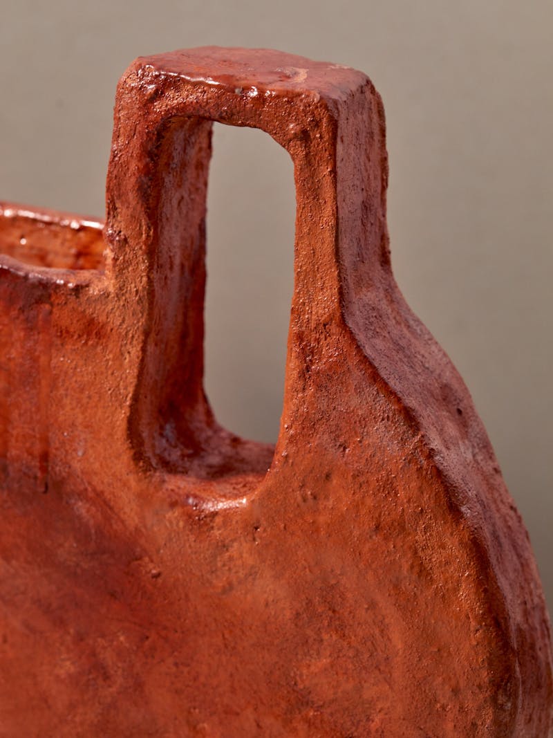 detail image of an orange flat ceramic vessel by Willem van Hooff with an oblong handle and irregular glaze