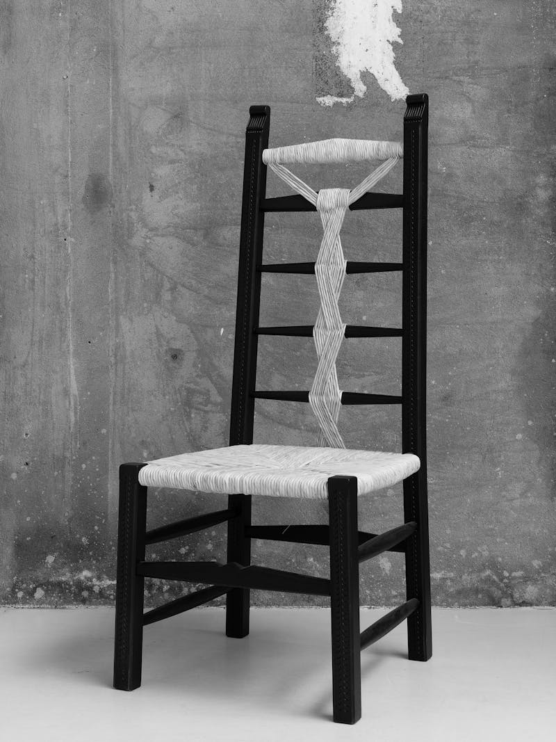 Black and white image displaying the Lia Chair from the 'scannu' series by Pretziada. The material is made from chestnut wood and contains woven decorative details. This object is part of the new 2024 spring collection 'Observations' by online gallery Metamorphoses Objects.