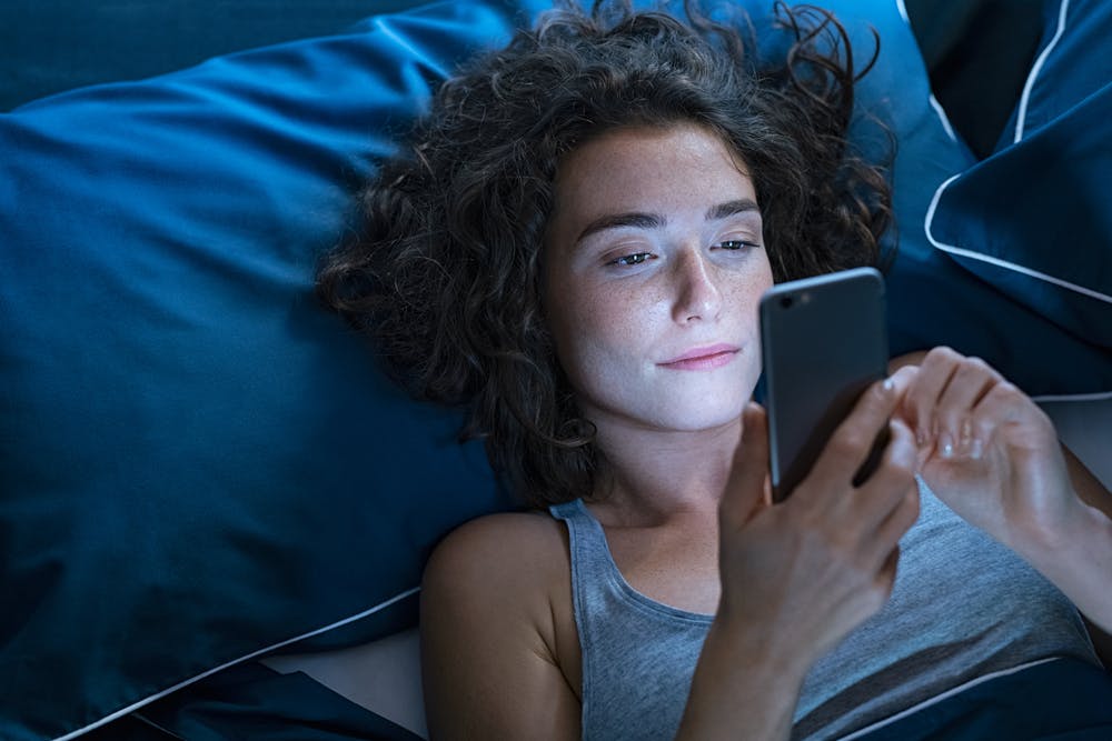 Woman pressing her phone at night instead of sleeping