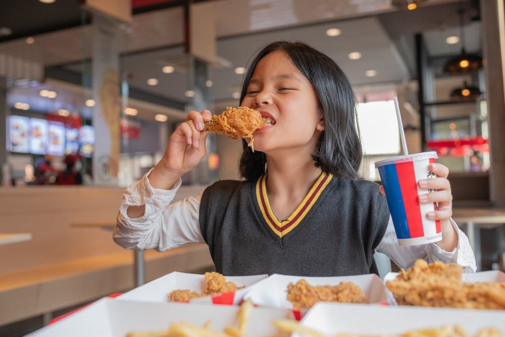 A young girl eating crisped fried chicken 