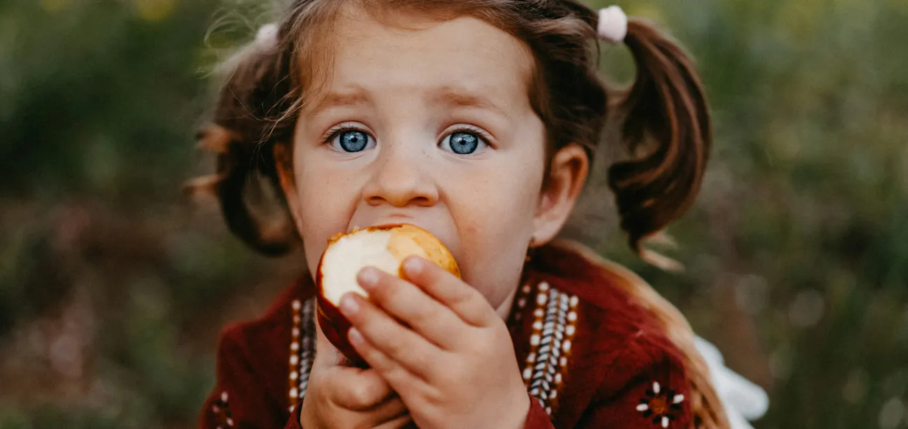 An image showing a pretty baby eating a fruit
