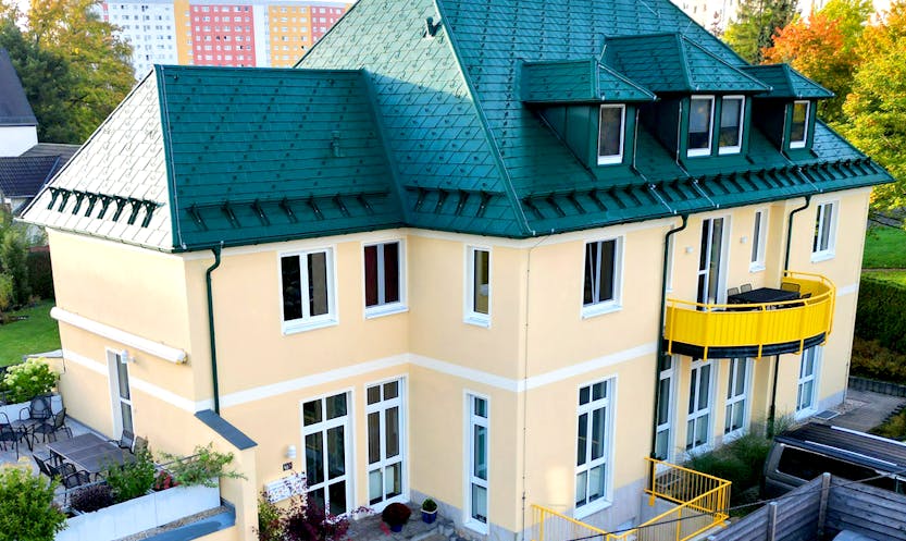 Gelbe Fassade an einem Mehrfamilienhaus mit grünem Dach. Malermeister Müller und Sohn