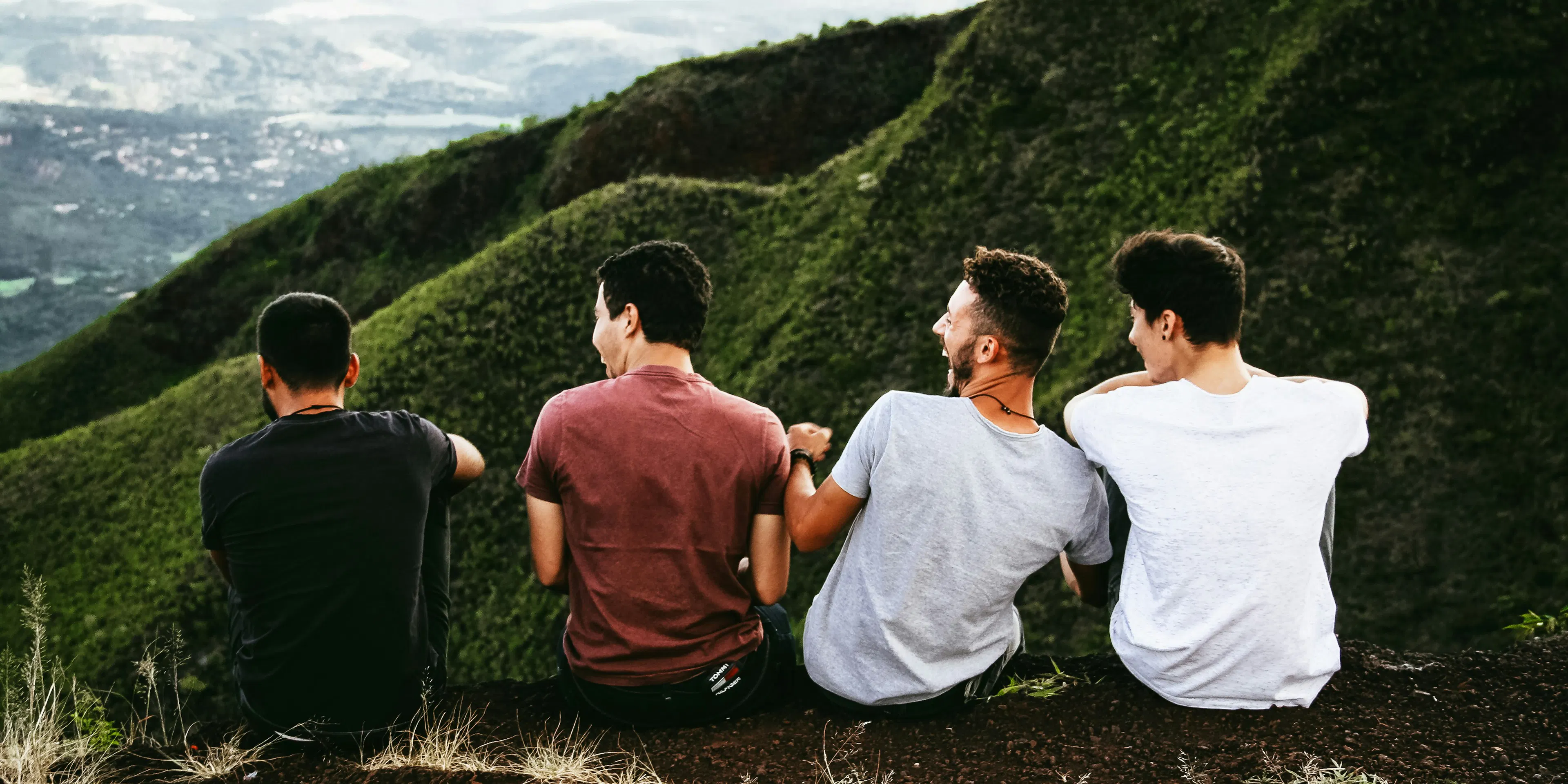 row of four men sitting on mountain trail