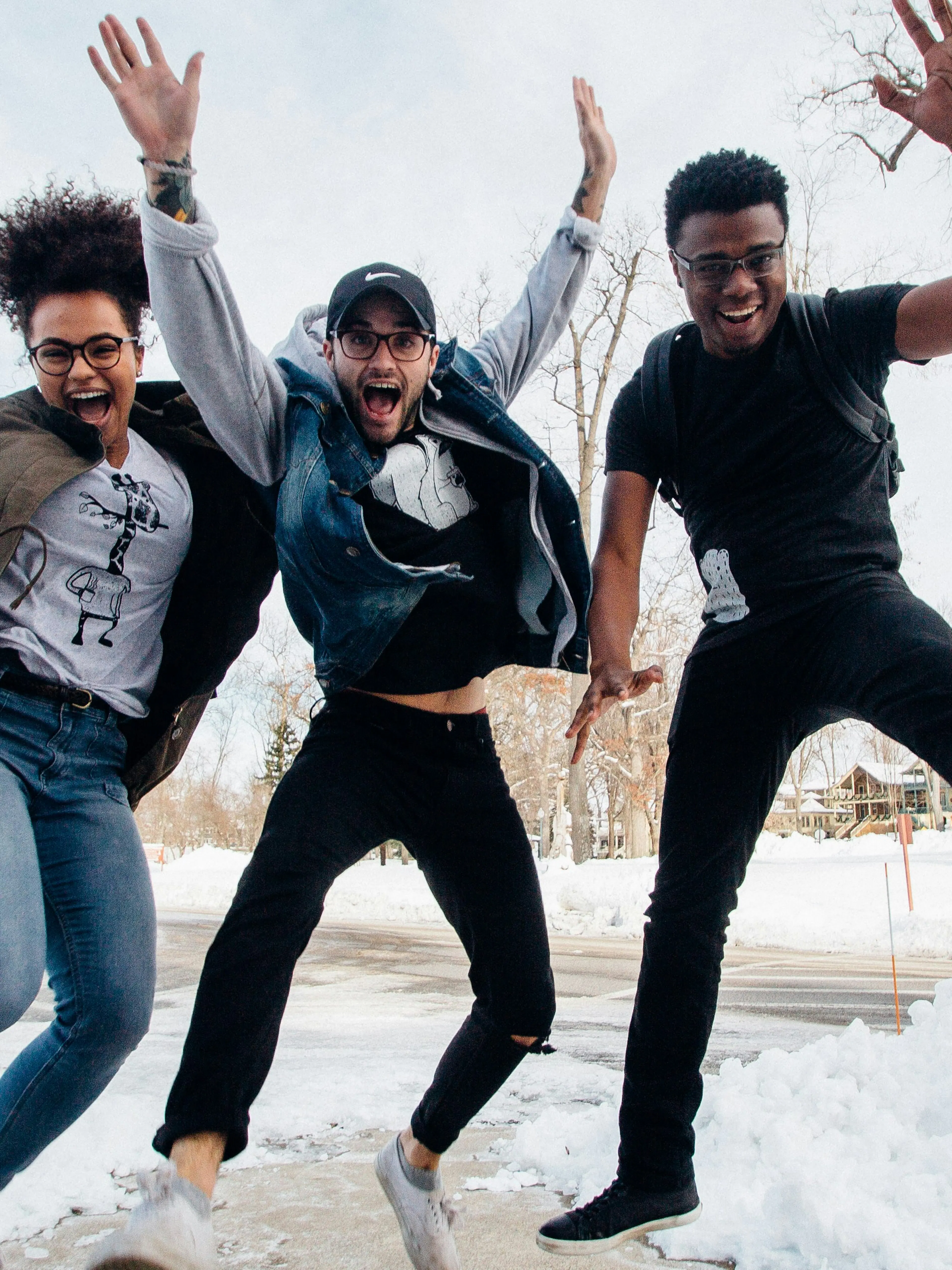 photo of three men jumping on ground near bare trees during daytime