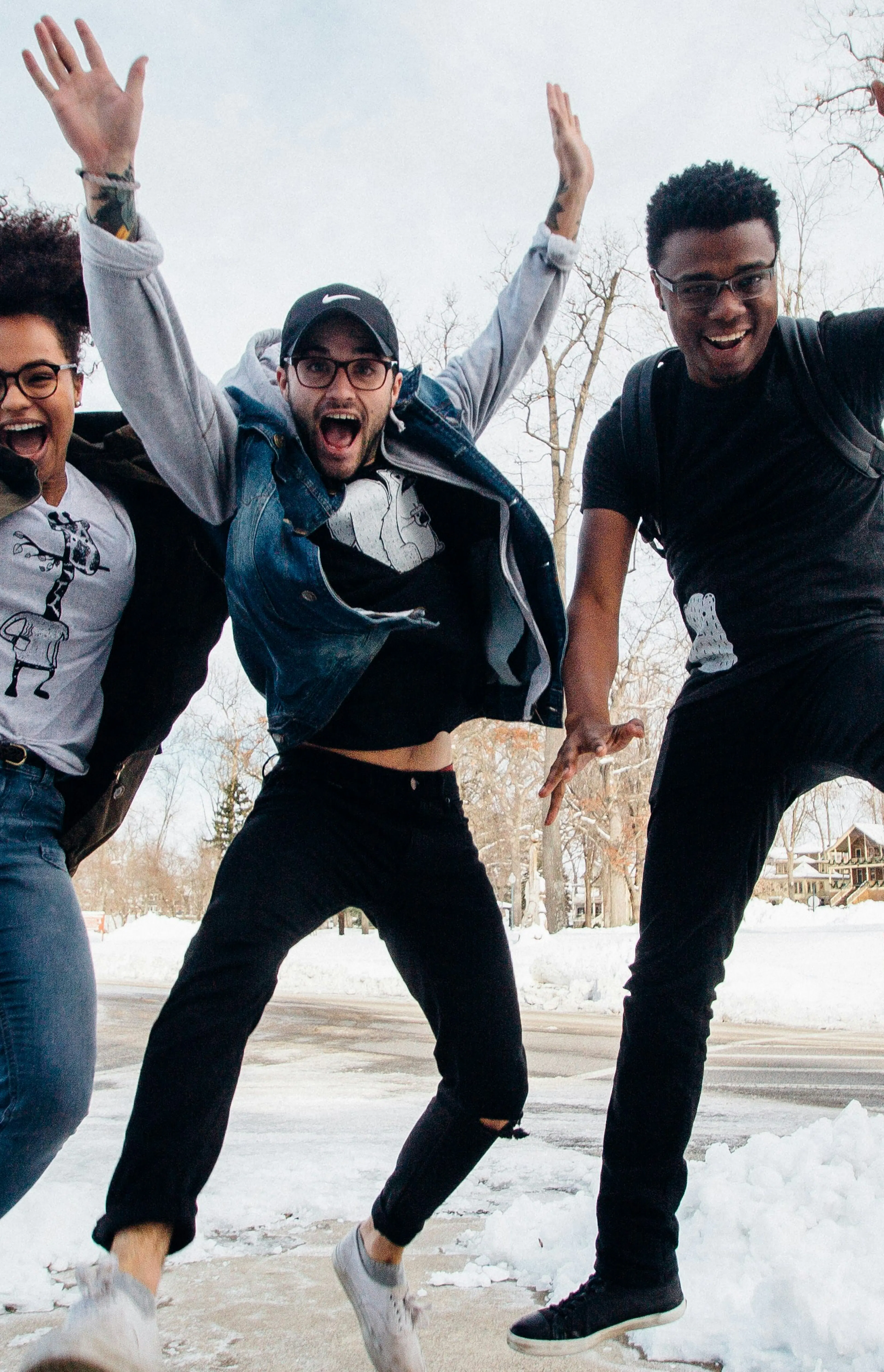 photo of three men jumping on ground near bare trees during daytime