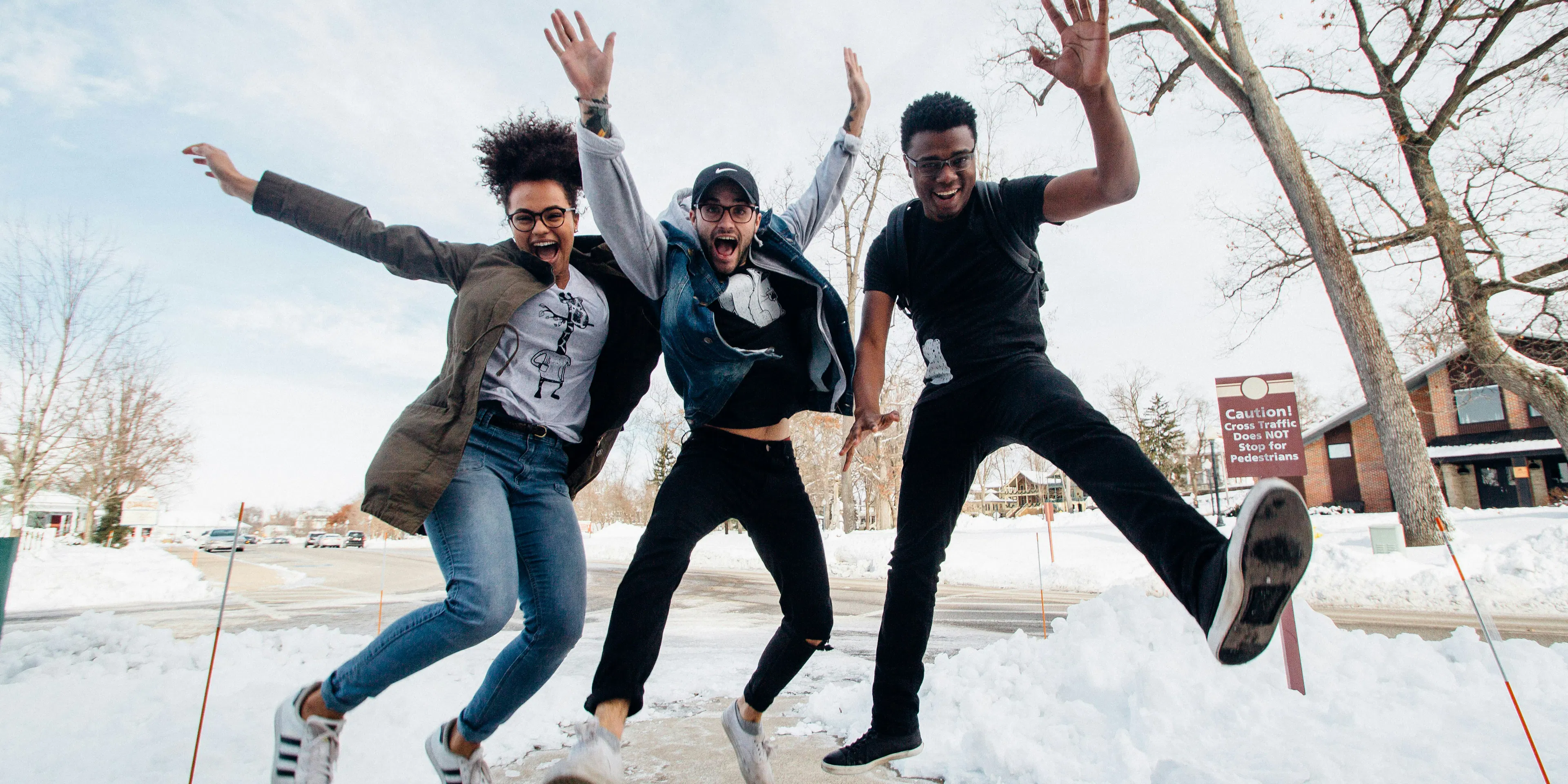 photo of three men jumping on ground near bare trees during daytime