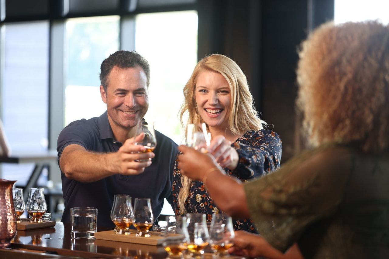Three people on a bourbon tour clinking glasses in a cheerful toast, enjoying their bourbon together.