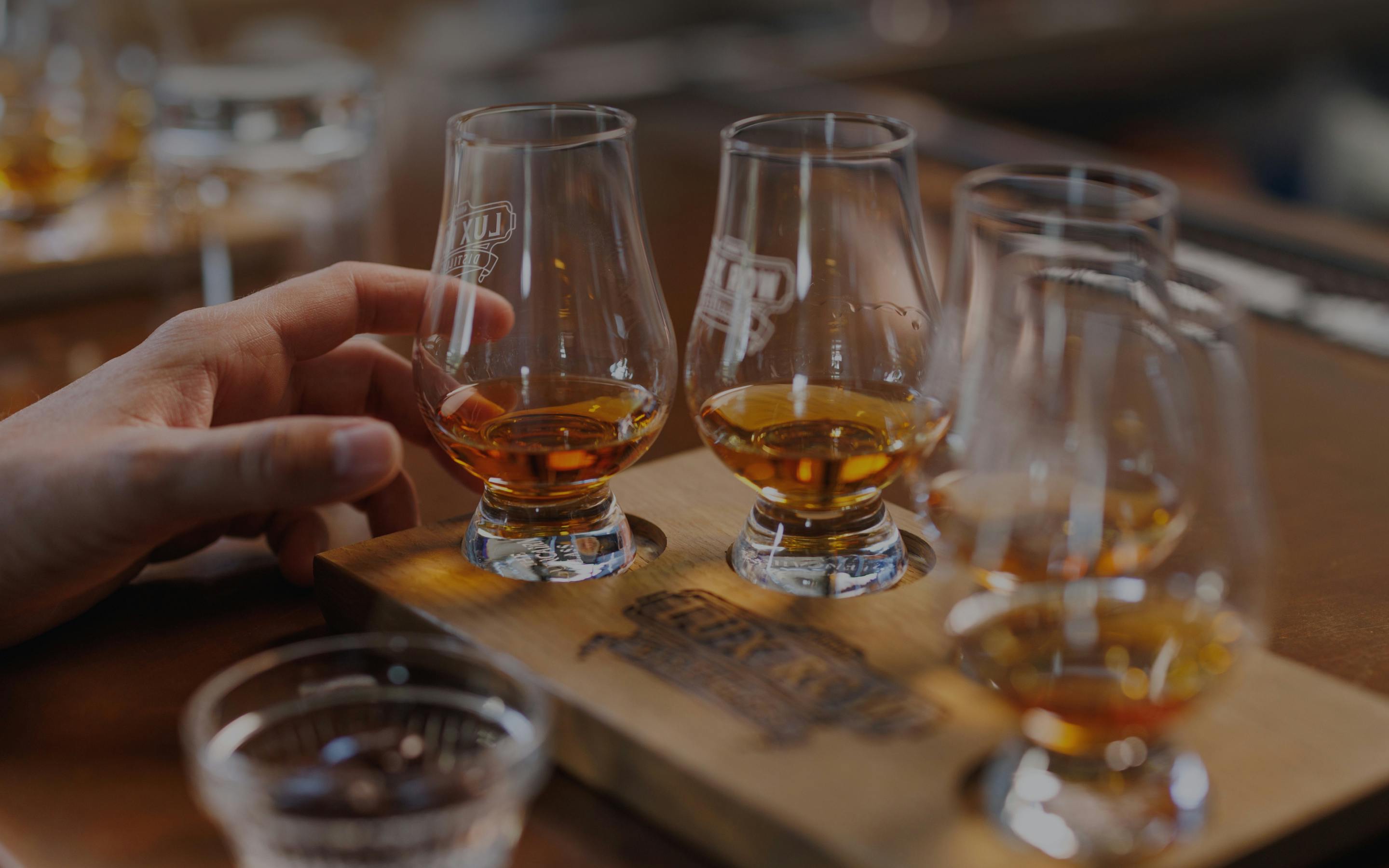 A set of glasses filled with whiskey, with a hand gently touching one.