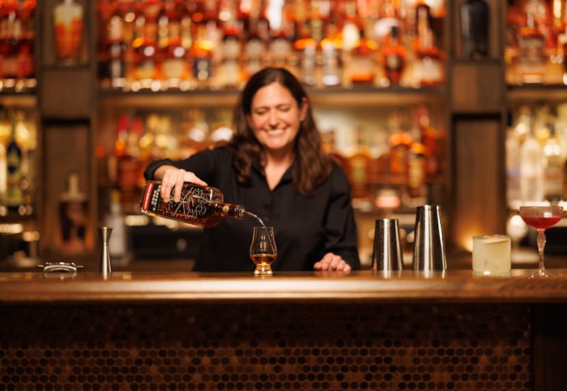 A female barista pouring a drink into a glass at a bar.