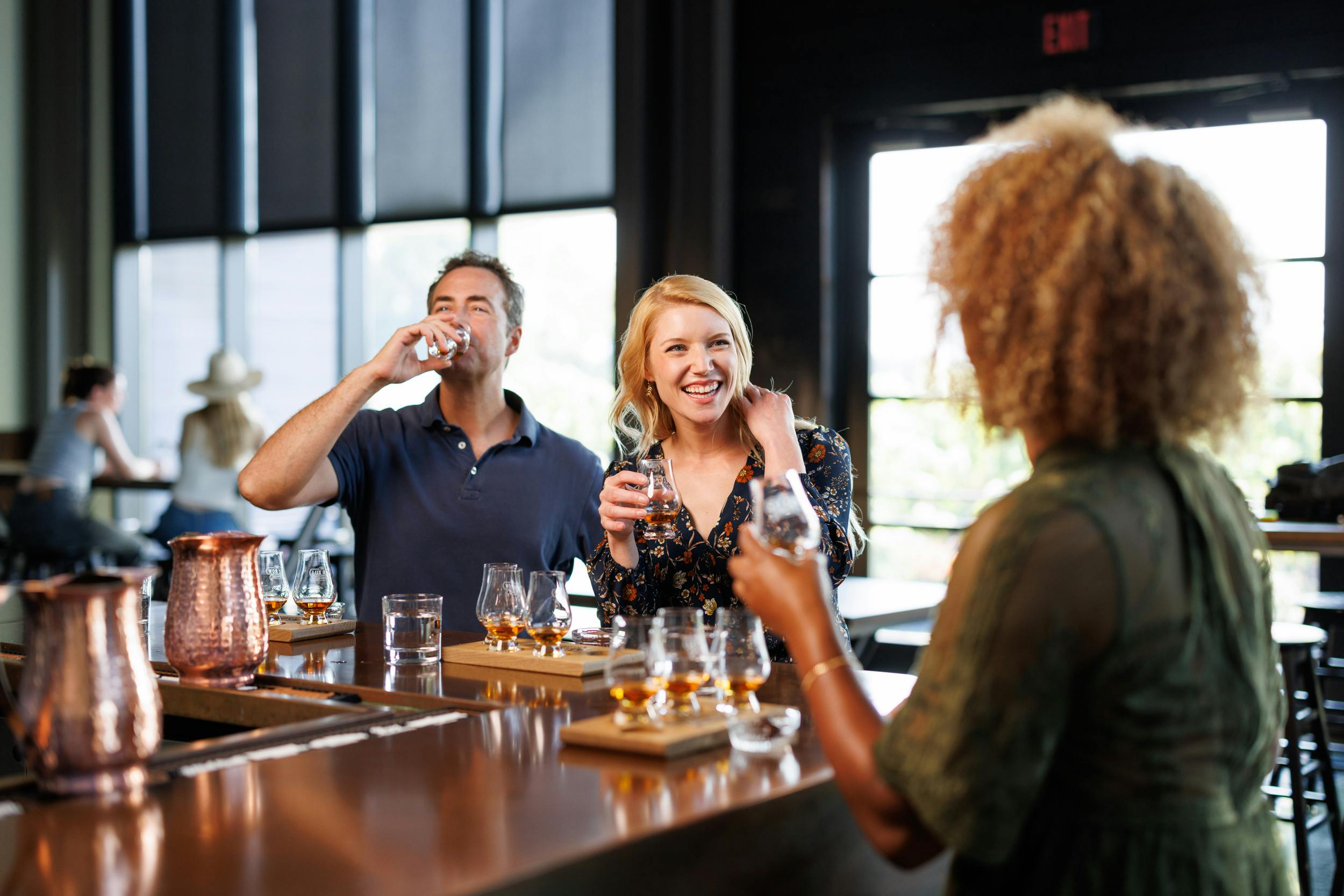 Three adults enjoying bourbon together at a bar.