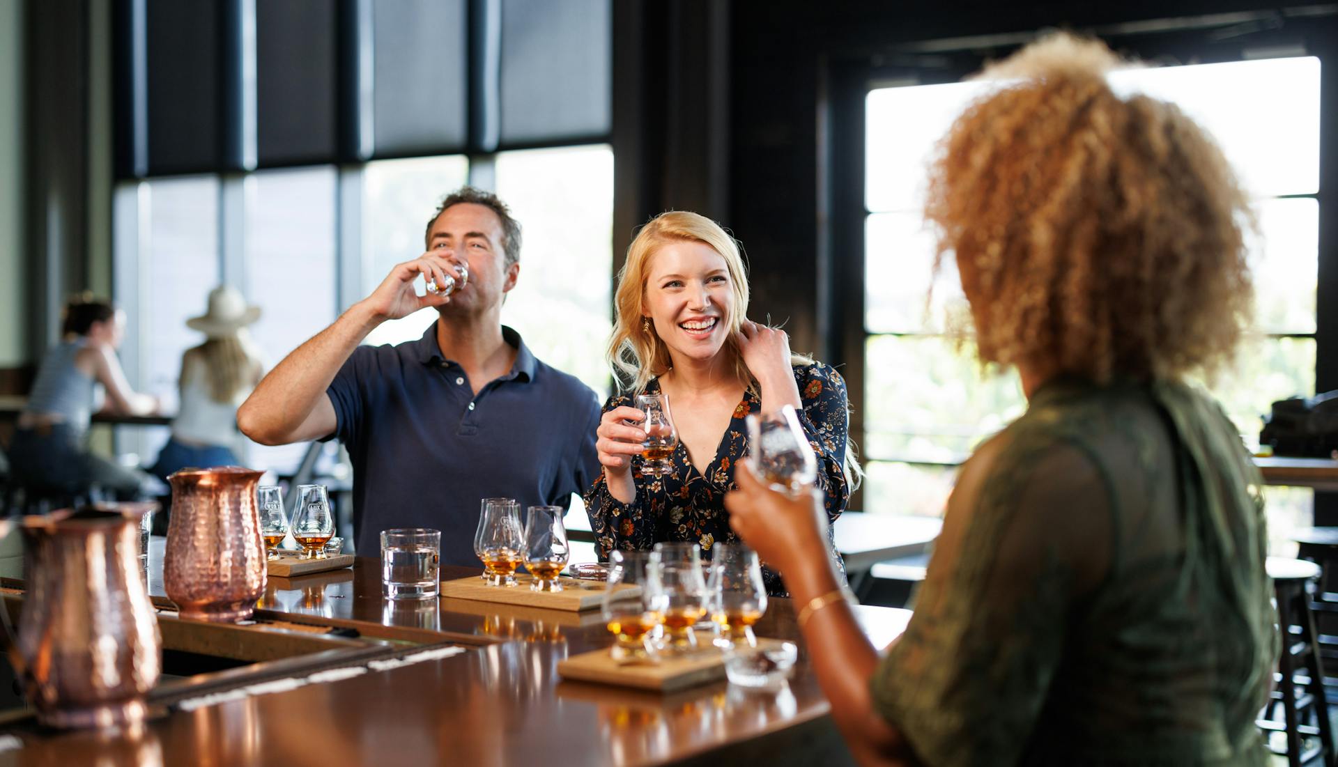 Three adults enjoying bourbon together at a bar.