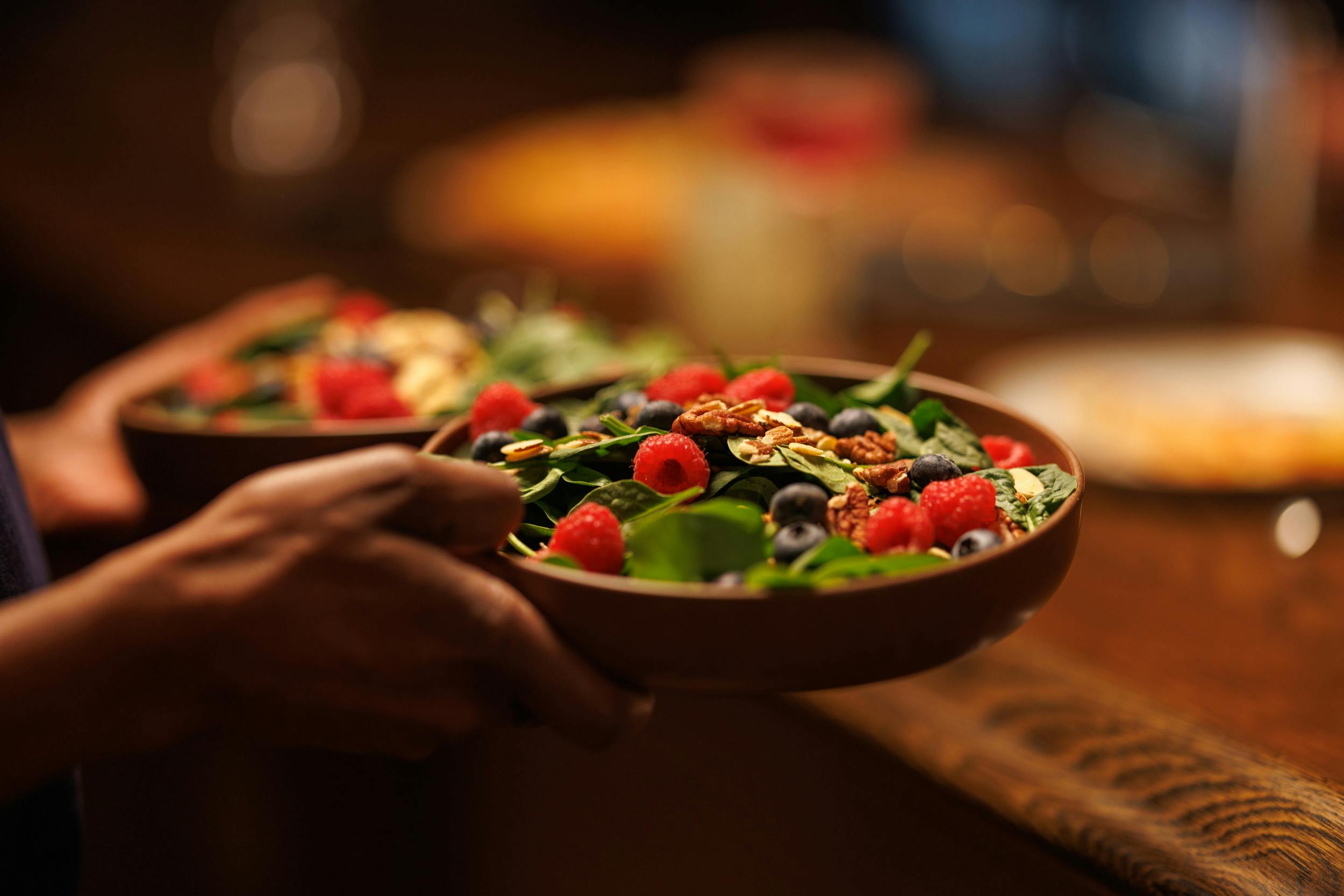 A hand holding a plate of fresh salad with a mix of greens and berries.
