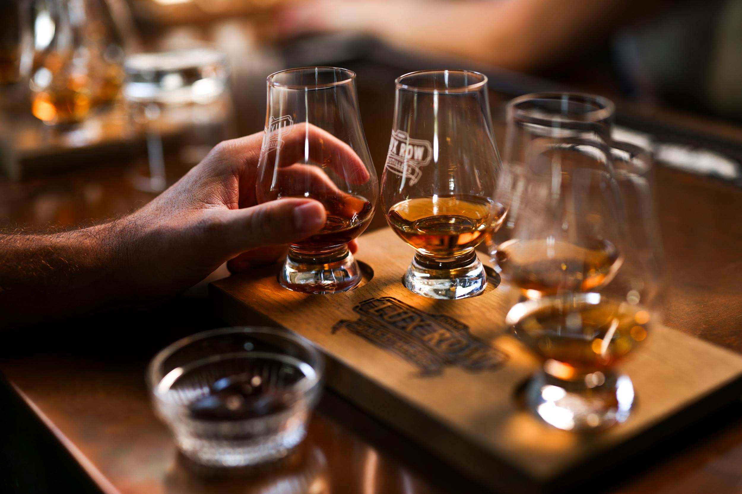 A set of glasses filled with bourbon, with a hand holding one of the glasses.