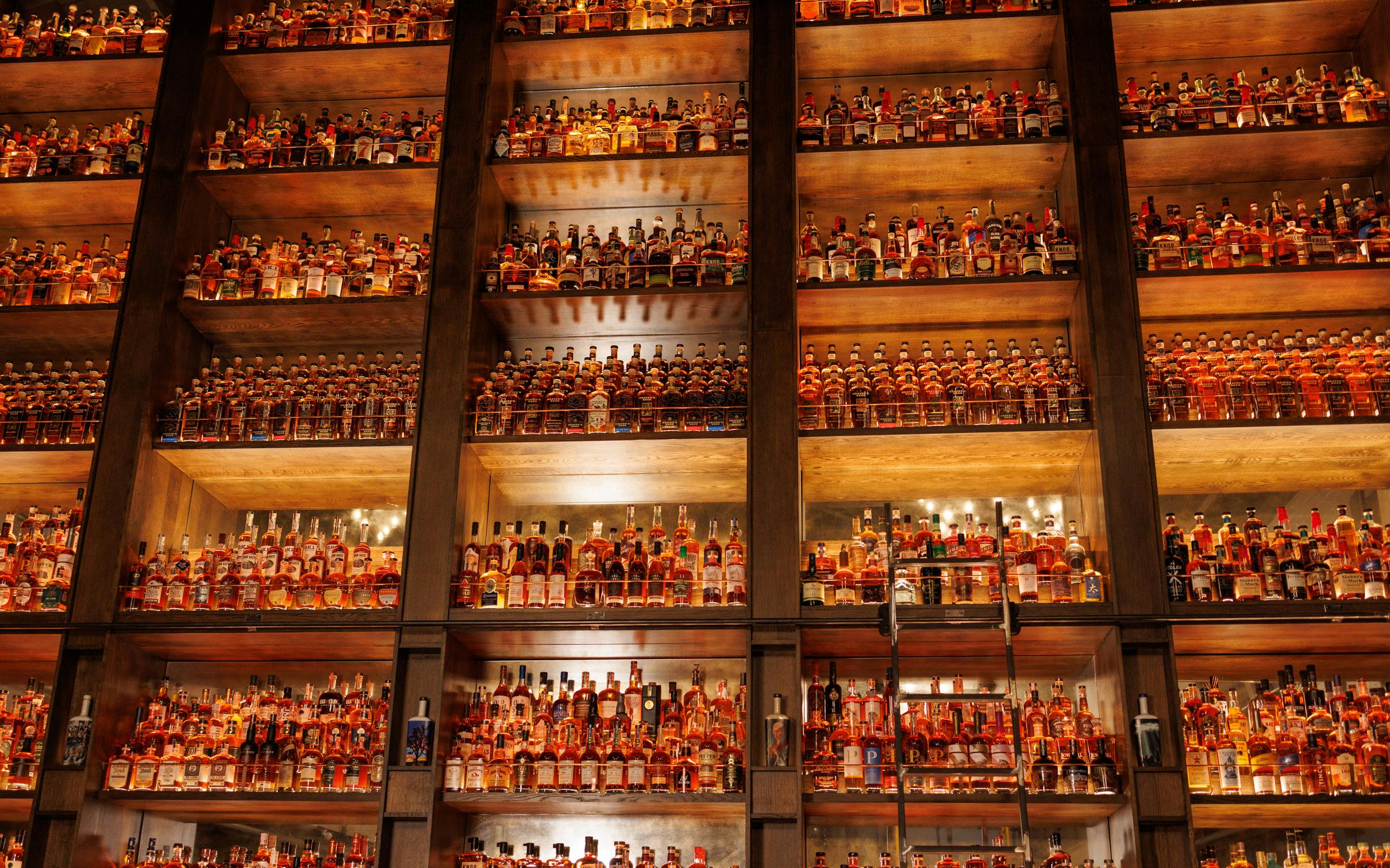 The High Church of Bourbon's wall of shelves holding numerous glasses of liquor, illuminated by amber-colored lights.