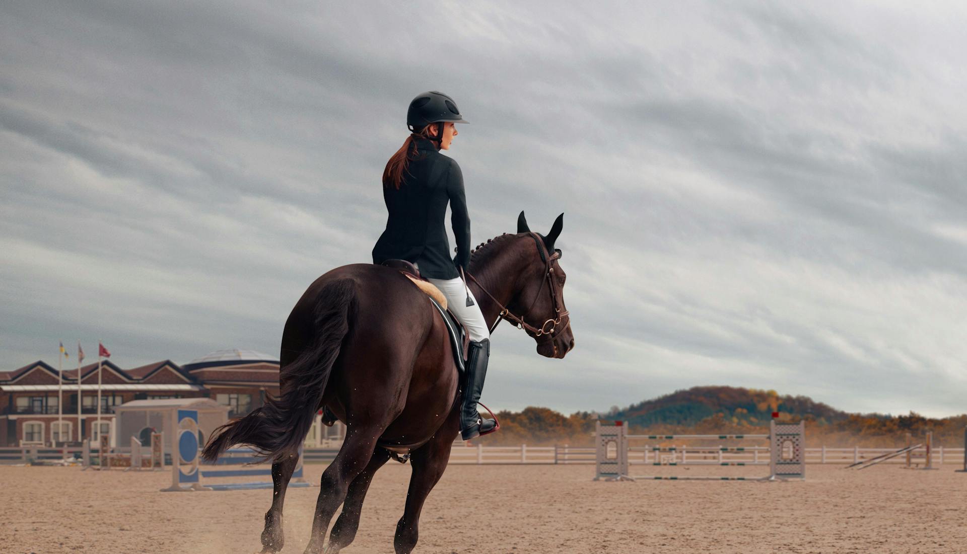 A woman horseback riding across a dusty field.