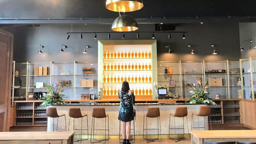 A woman standing at an empty bar at Angel’s Envy Distillery, surrounded by the distillery's elegant interior.