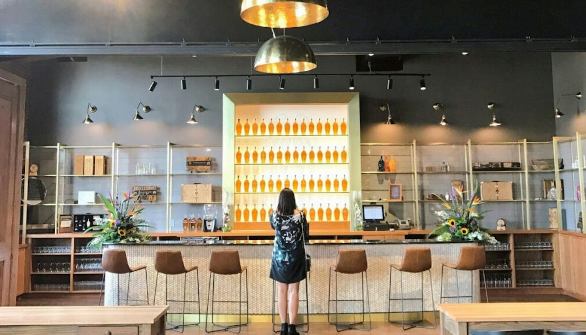 A woman sitting at an empty bar at Angel’s Envy Distillery, surrounded by the distillery's elegant interior.