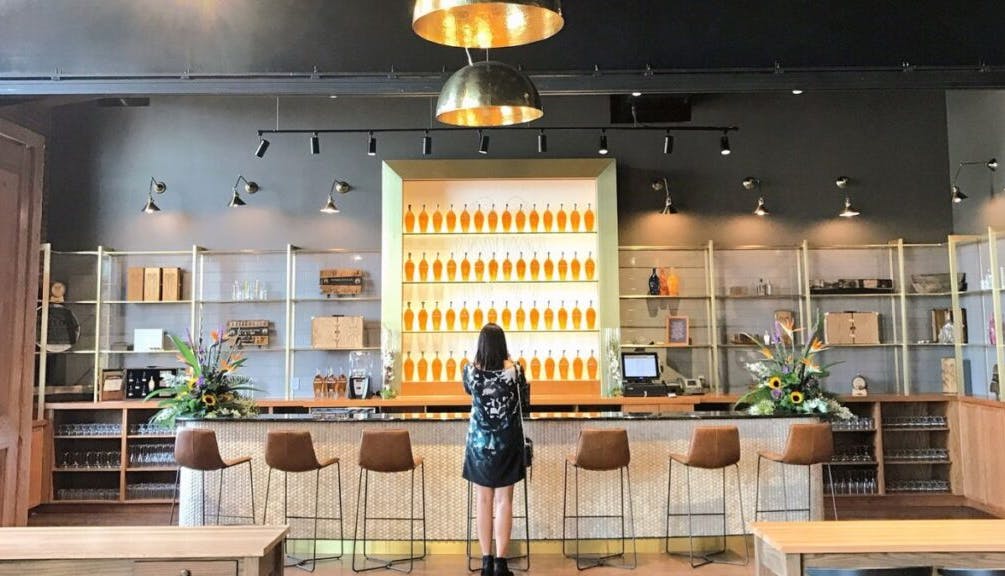 A woman sitting at an empty bar at Angel’s Envy Distillery, surrounded by the distillery's elegant interior.