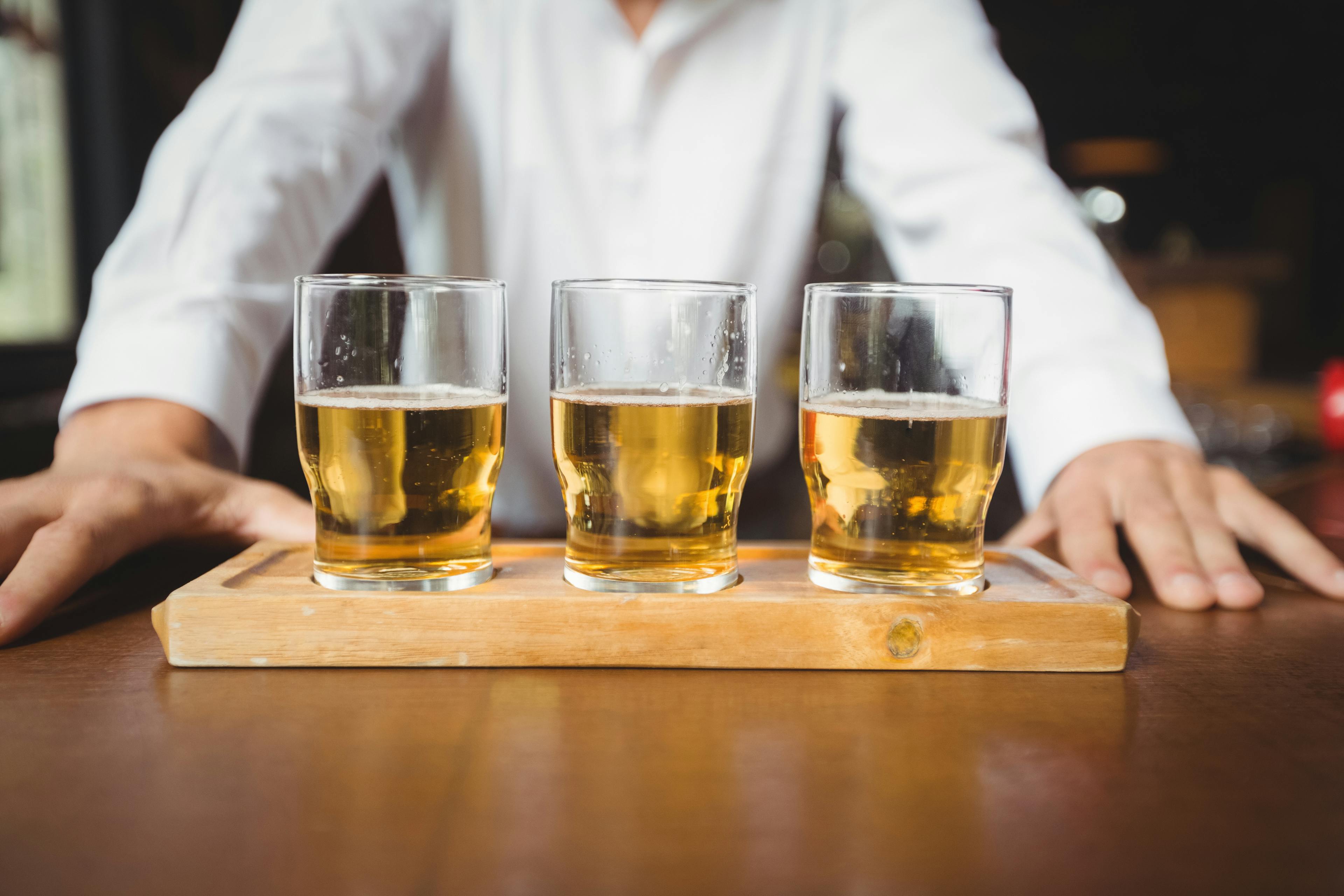 A man presenting a tray containing a set of drinks.