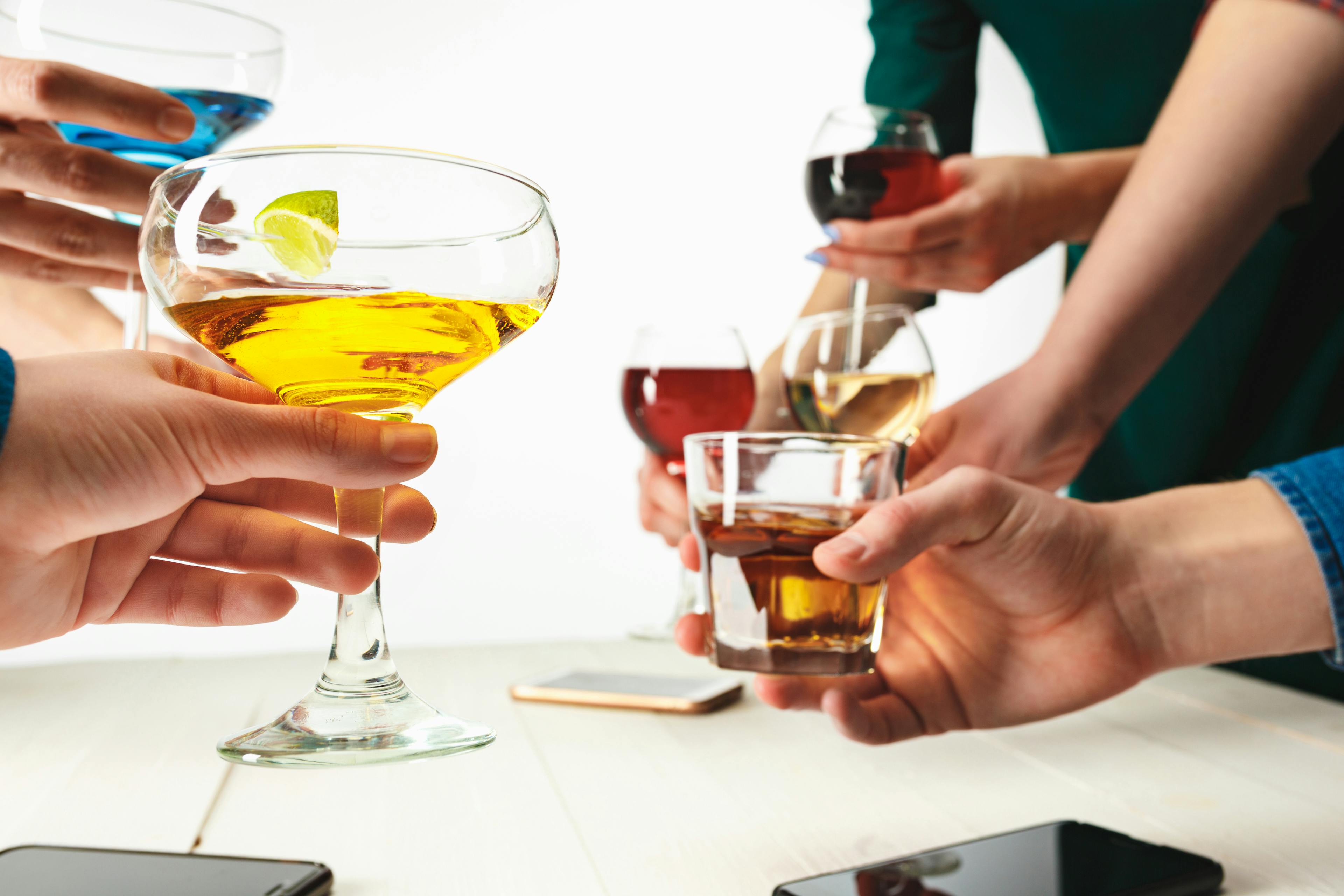 Hands holding a variety of drinks, showcasing different colors and glass styles.