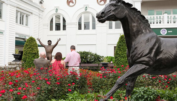 An exterior view of Churchill Downs, featuring the horse statue at the entrance, with lush green grounds and the grand entrance welcoming visitors to the historic racetrack.