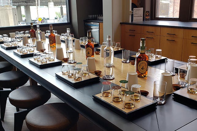 A large table with sets of drinking glasses, each containing samples of bourbon.