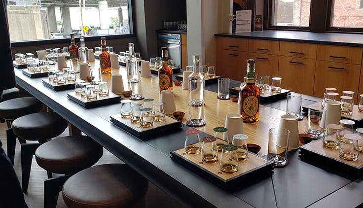A large table with sets of drinking glasses, each containing samples of bourbon.