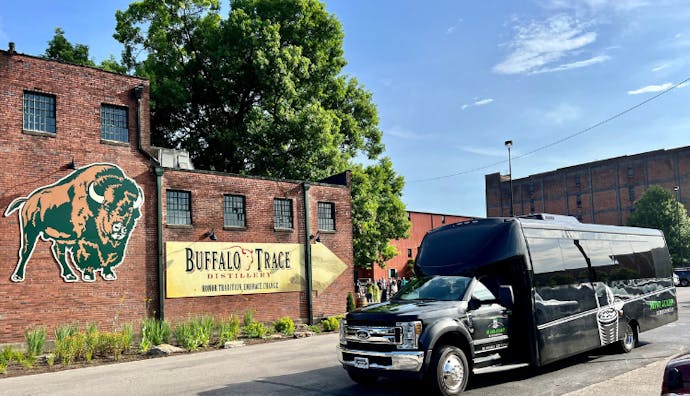 A Mint Julep Experiences luxury vehicle parked in front of Buffalo Trace Distillery, with the historic brick buildings and iconic signage visible in the background.