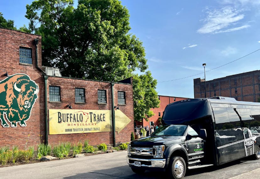 A Mint Julep Experiences luxury vehicle parked in front of Buffalo Trace Distillery, with the historic brick buildings and iconic signage visible in the background.