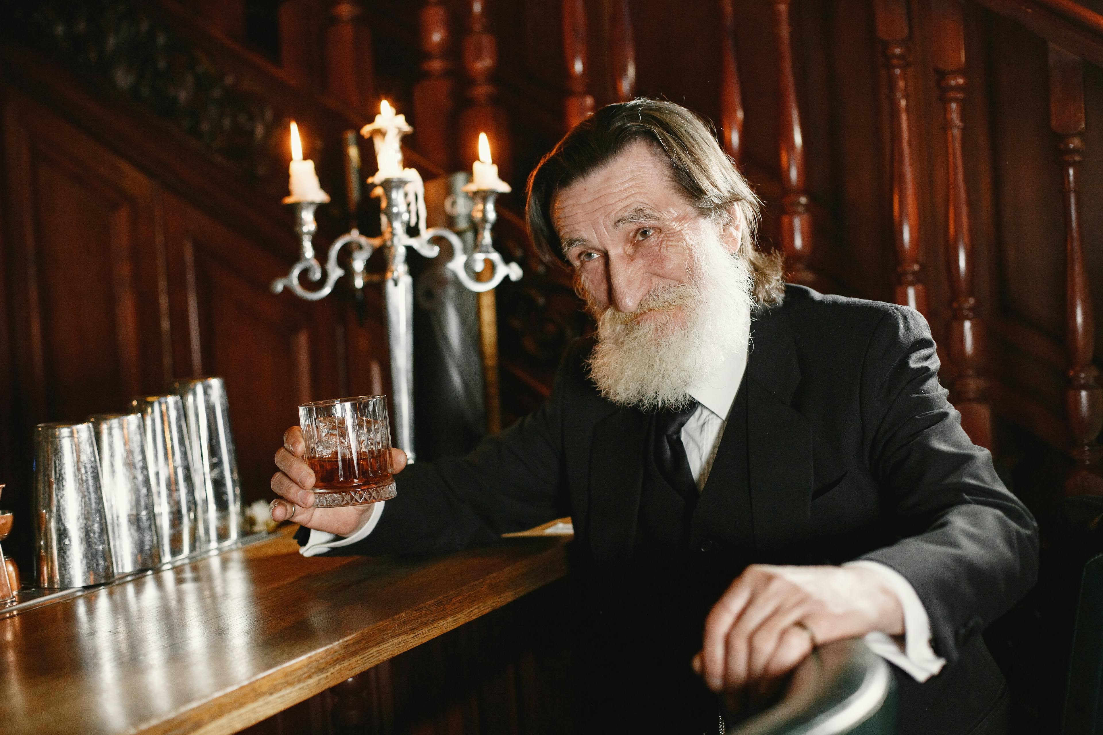 "An elderly man with a white beard, holding a glass of bourbon, set against an antique backdrop.